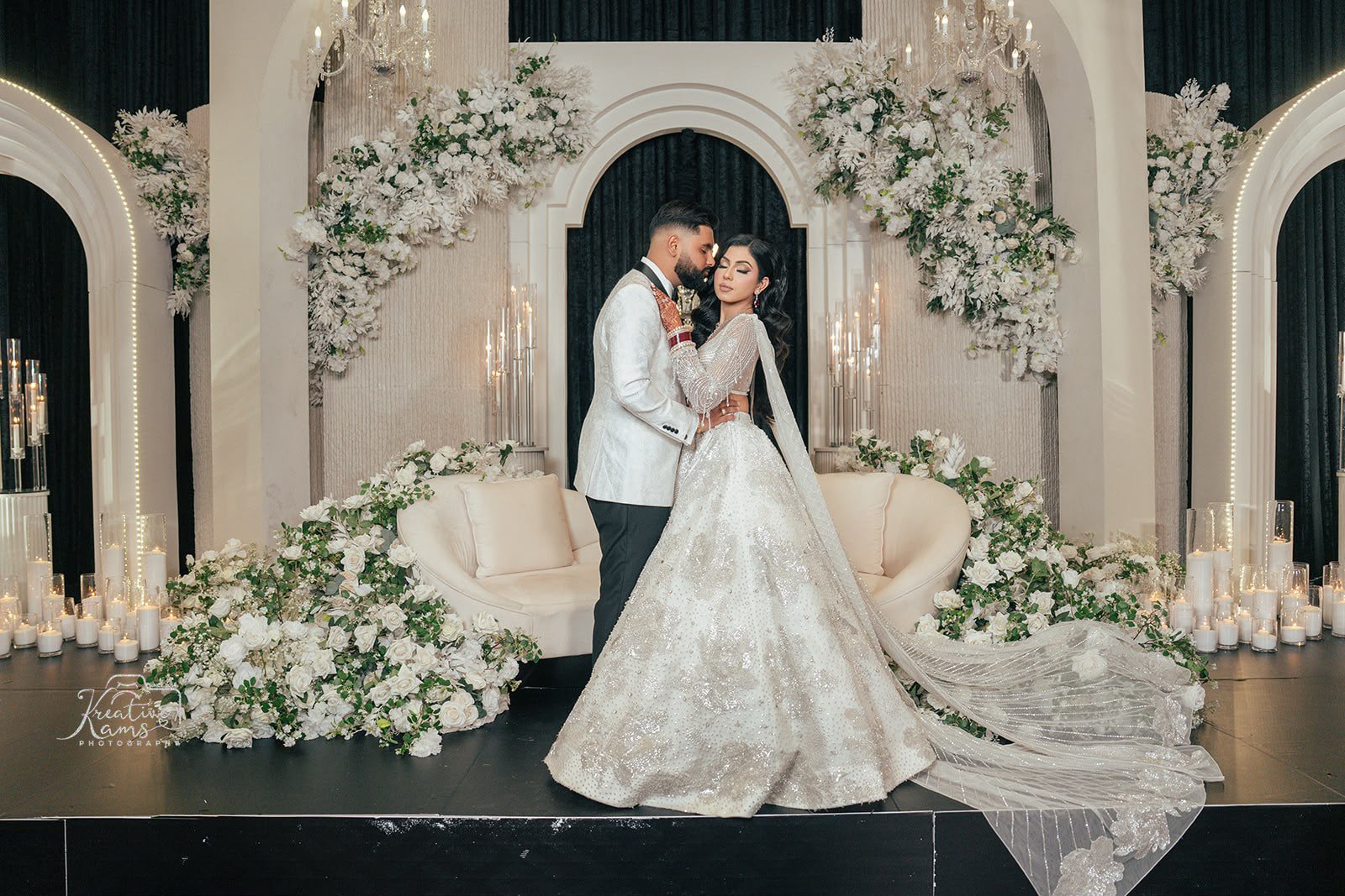 A newlywed couple standing together among white floral wedding decor